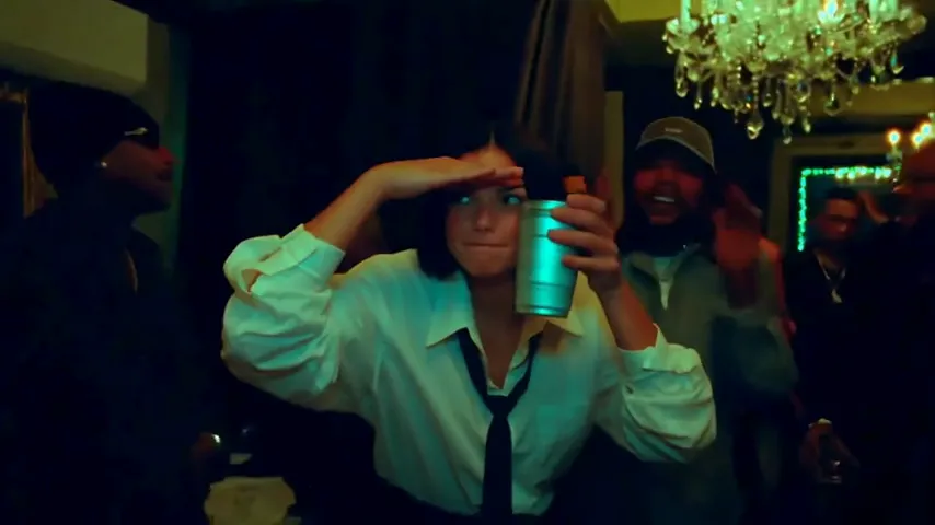 A frame from a Drake Burning Bridges AI video: the host does the hand-over-the-eyes move under the chandeliers